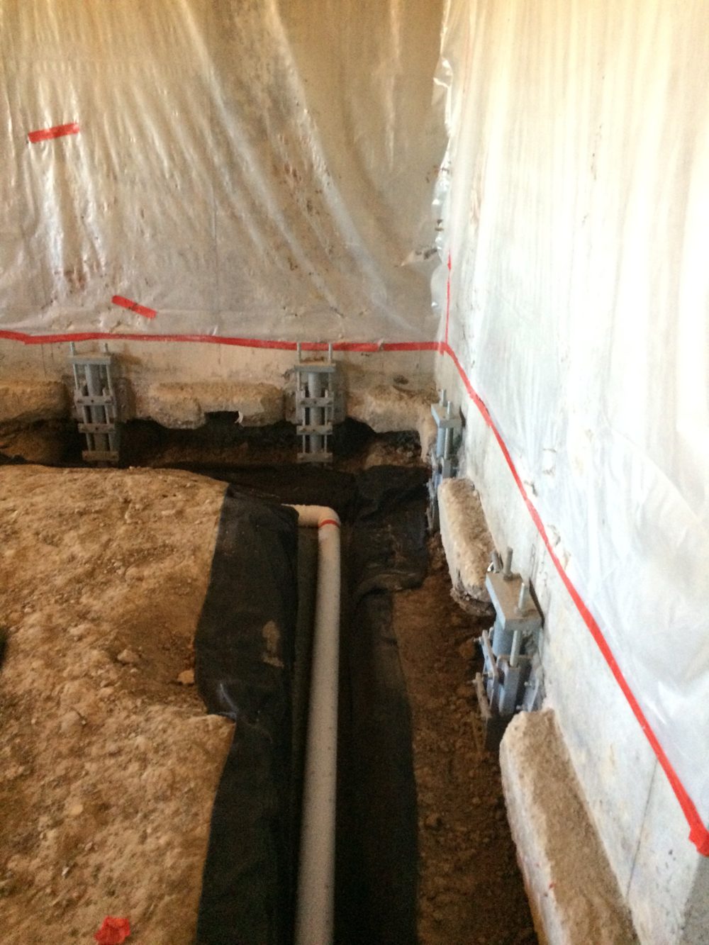 Underpinning brackets along a basement foundation wall beside a new interior drain