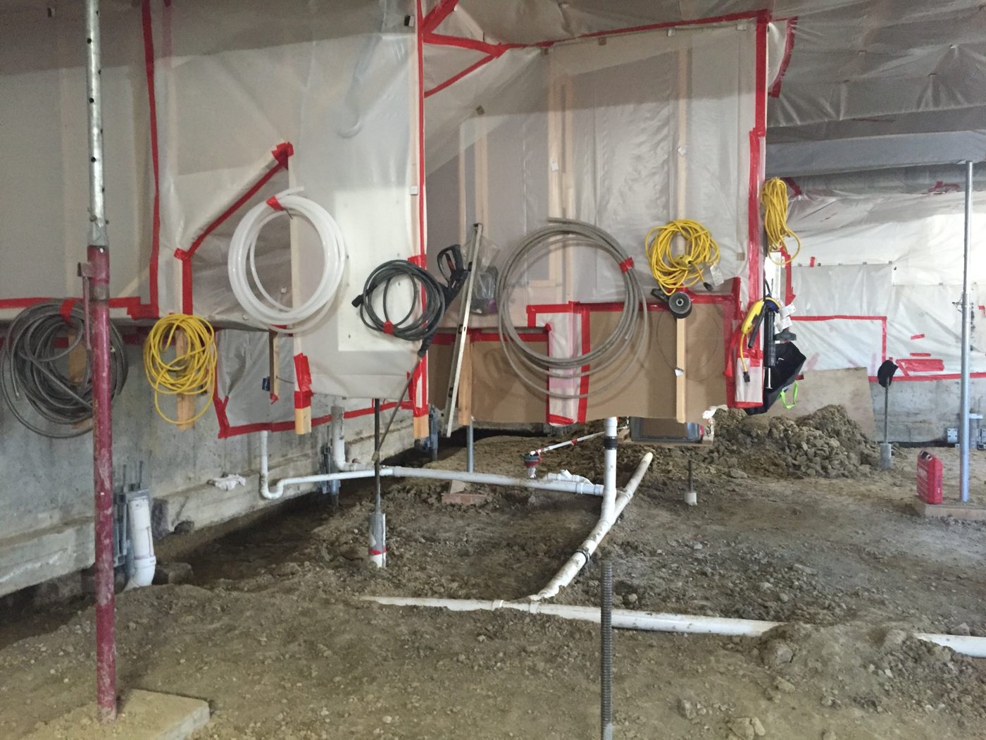 Basement protected with plastic sheeting during underpinning, with shoring posts and new under-slab plumbing in place