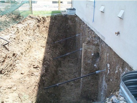 Helical tiebacks installed through a home's foundation wall in an open excavation
