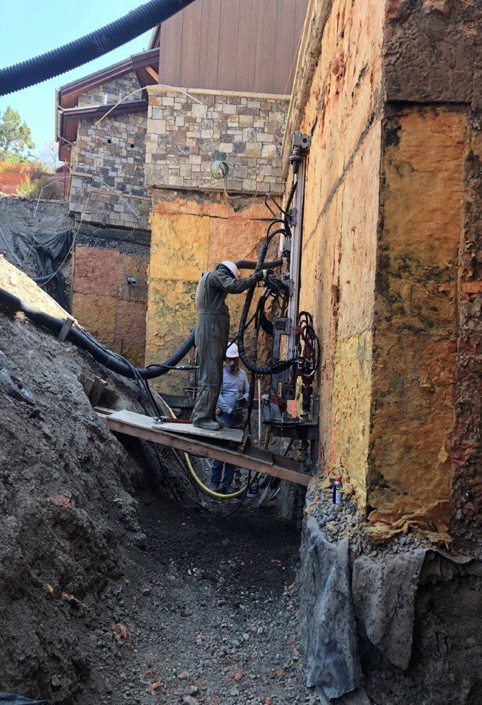 Park Range crew running a micropile drill along the foundation wall of a large stone home at Ridgeway